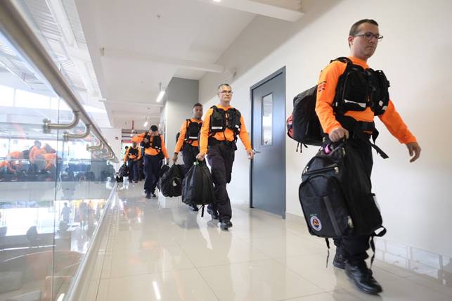 Rescatistas caminan por un pasillo del nuevo edificio de la academia nacional de bomberos, con su uniforme anaranjado, su equipo y un bulto.