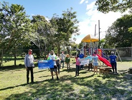 Un grupo de personas en un parque, aparece un parque infantil de colores y las personas están viendo al frente sosteniendo carteles.